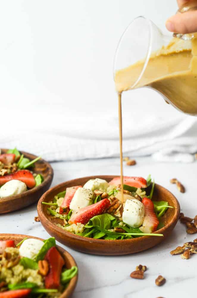 pour shot of creamy balsamic being poured from small pitcher onto salad that's plated on wooden plate