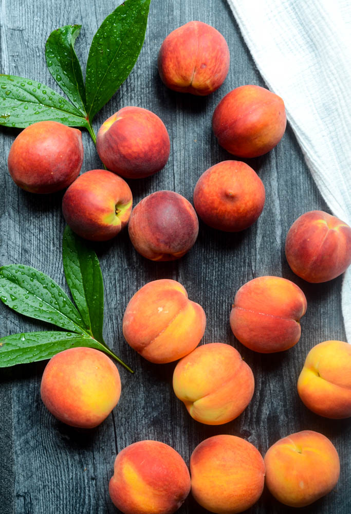 aerial view of peaches against a black wooden backdrop with green leaves. 