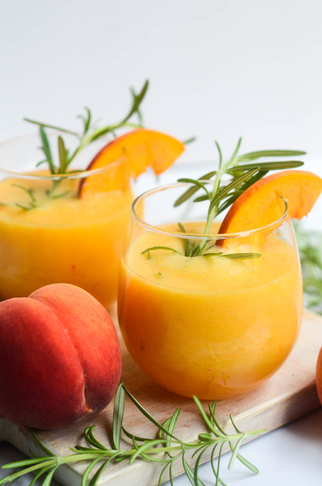 up close side picture of peach bourbon cocktail on a wooden cutting board next to a peach