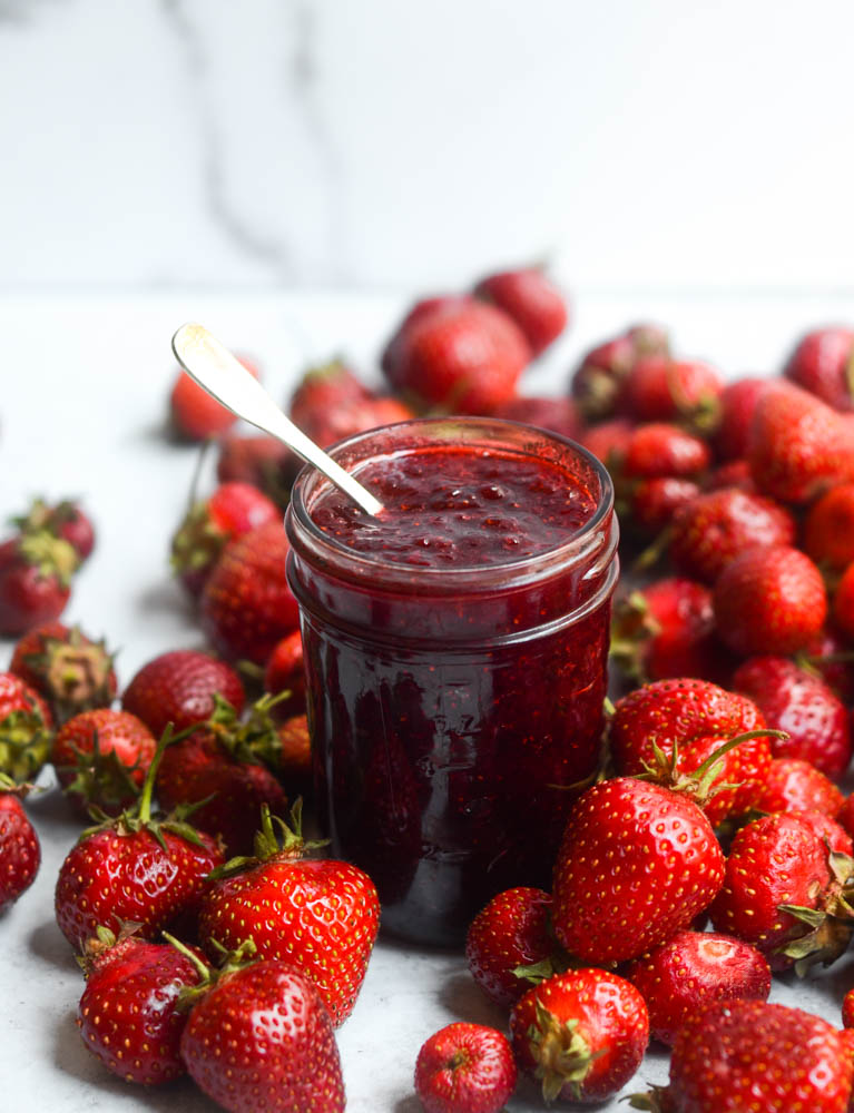 side view of jar of strawberry jam with fresh strawberries all around the jar