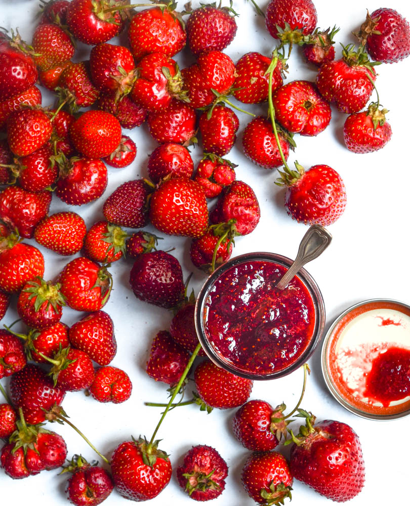 aerial shot of strawberry jam with strawberries against a white background and spoon in jam