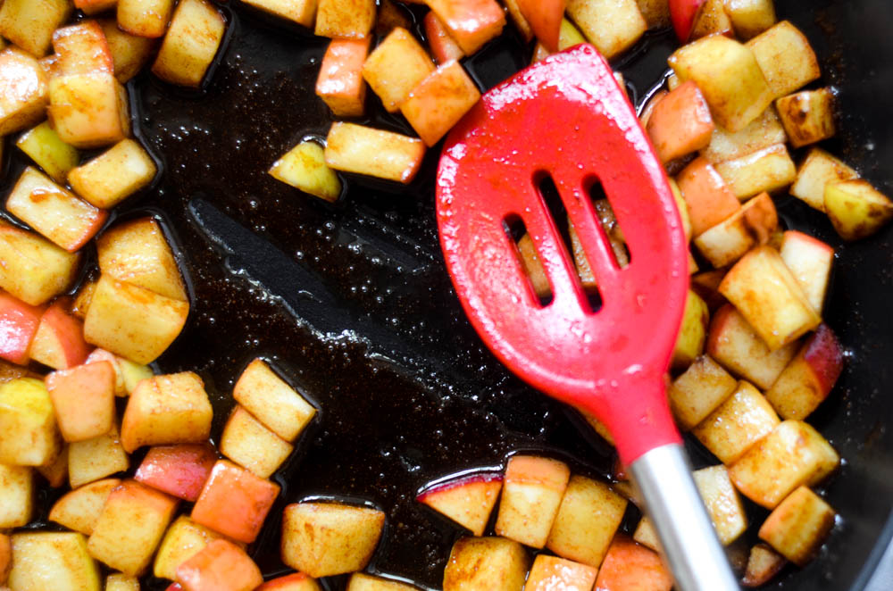 close up picture of apples cooking on non-stick skillet with red spatula