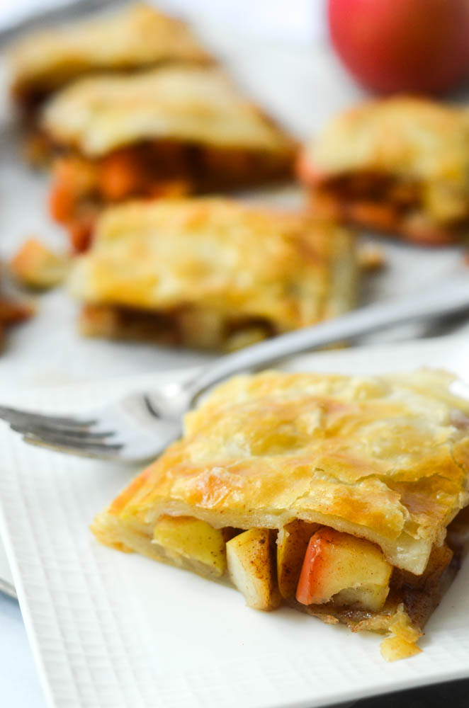 close up picture of apple slab pie with puff pastry on white plate with fork in background