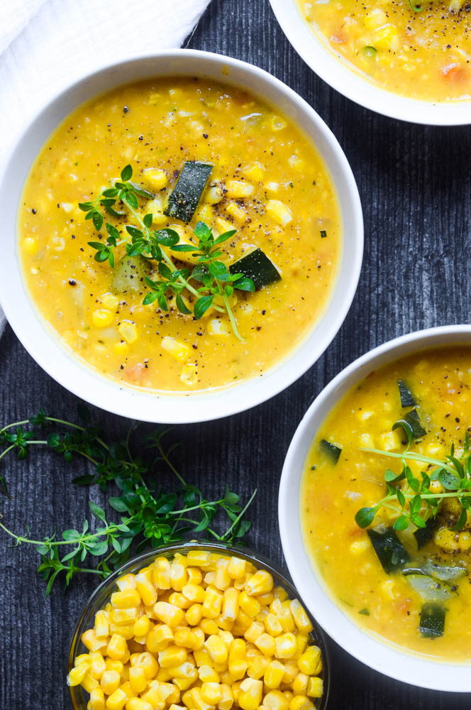 up close aerial picture of corn and zucchini chowder in three white bowls against black wooden background with fresh thyme