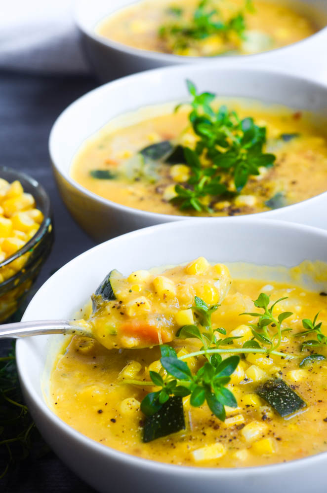 up close picture of spoonful of corn and zucchini chowder with other bowls of soup in background