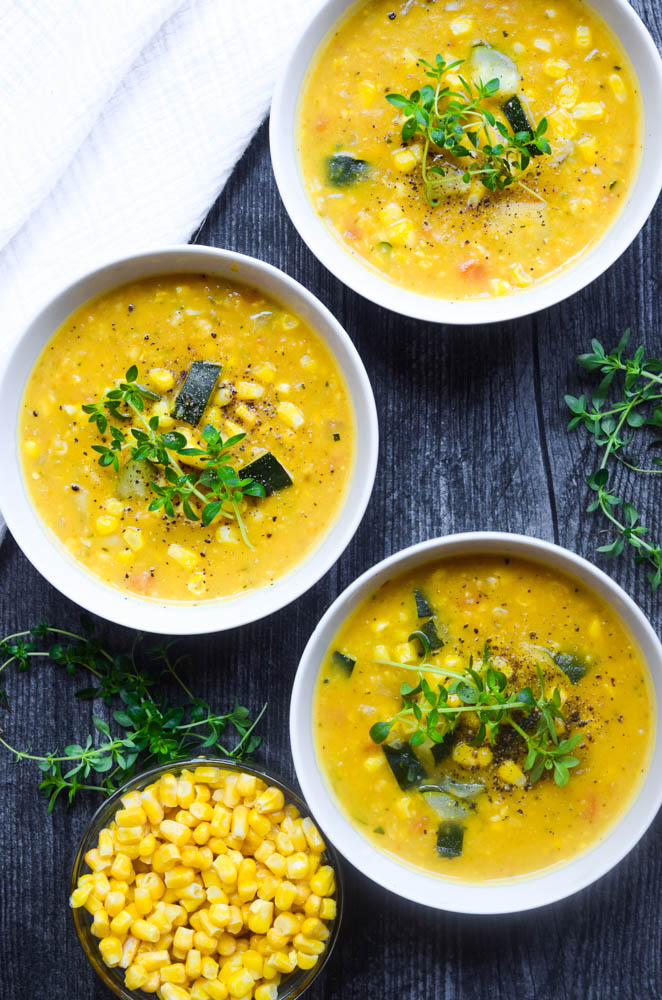 flat lay of three bowls of soup with bowl of corn in bowl and thyme scattered 