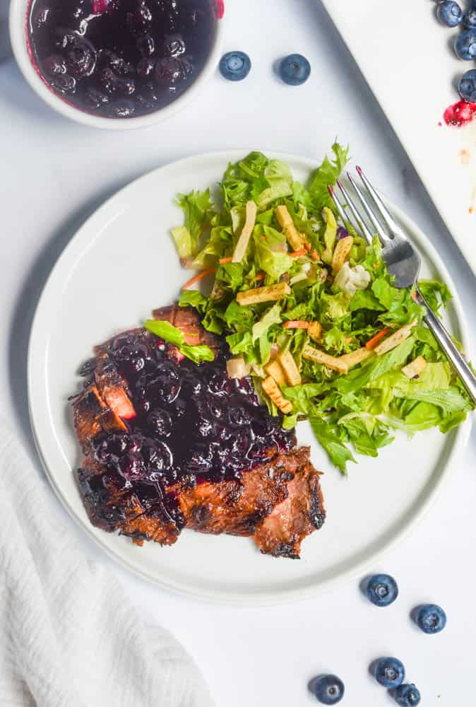 aerial shot of white plate with flank steak with blueberry sauce and side salad.  