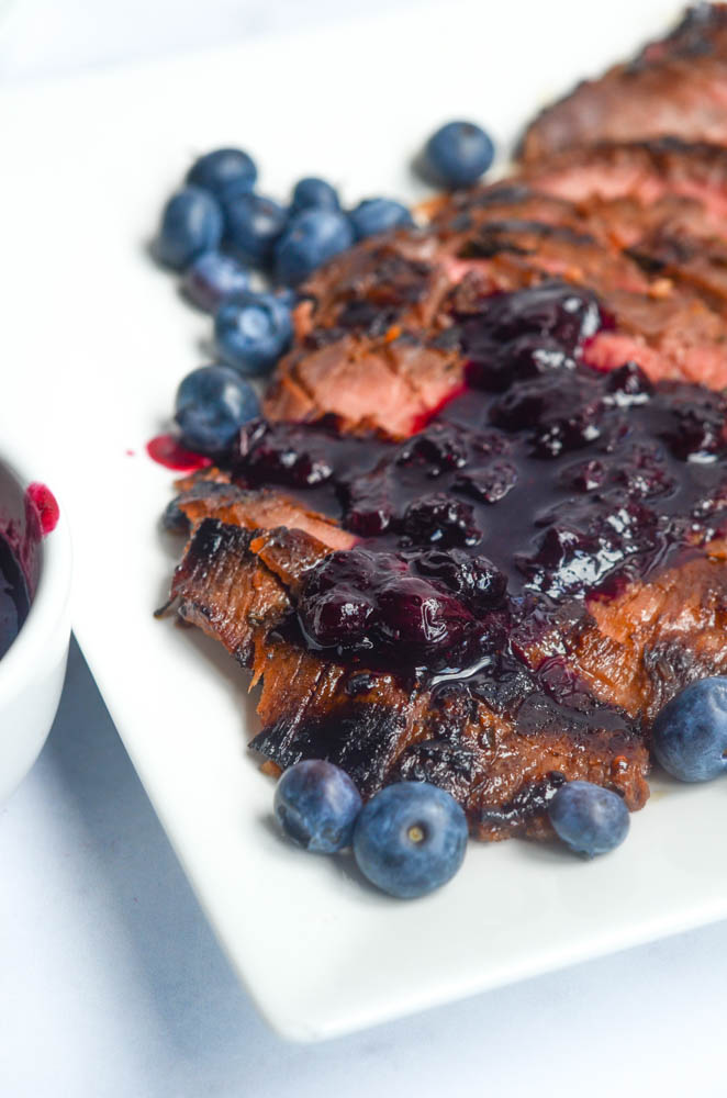 up close picture of sliced flank steak with blueberry sauce