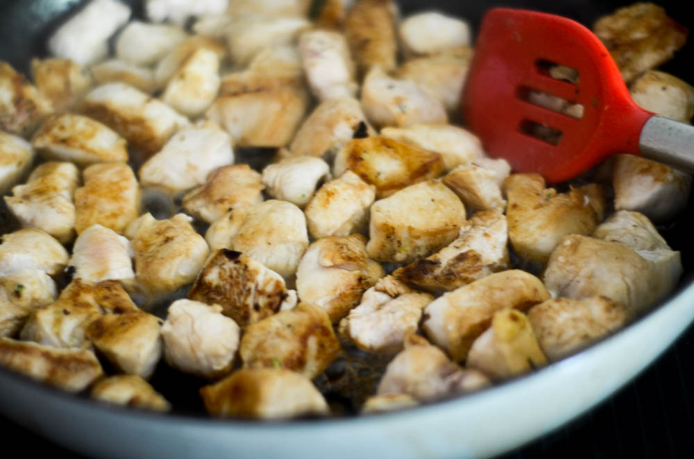 close up picture of chicken cooking in a cast iron skillet with red spatula