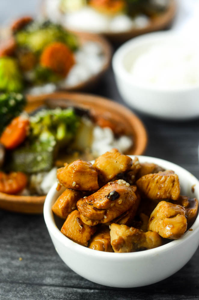 close up angle of bowl of hibachi chicken in white bowl with plate of vegetables in background