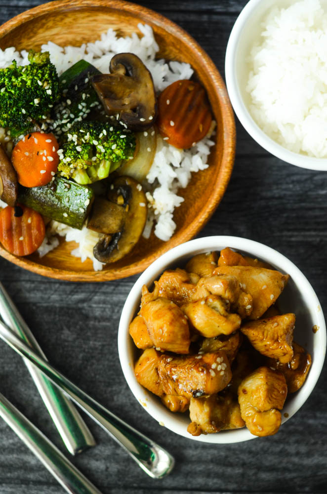 overhead shot of hibachi chicken in white bowl with sesame seeds on top and a plate of stir fry vegetables with rice on the side. 