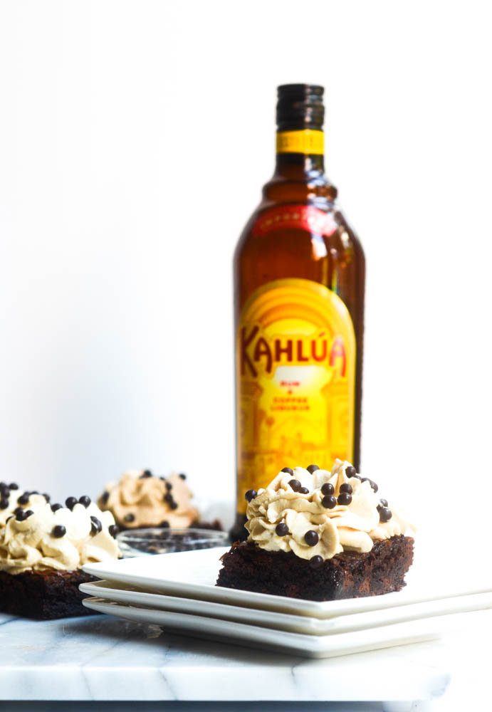 brownie with frosting on stack of white plates with kahlua bottle in background