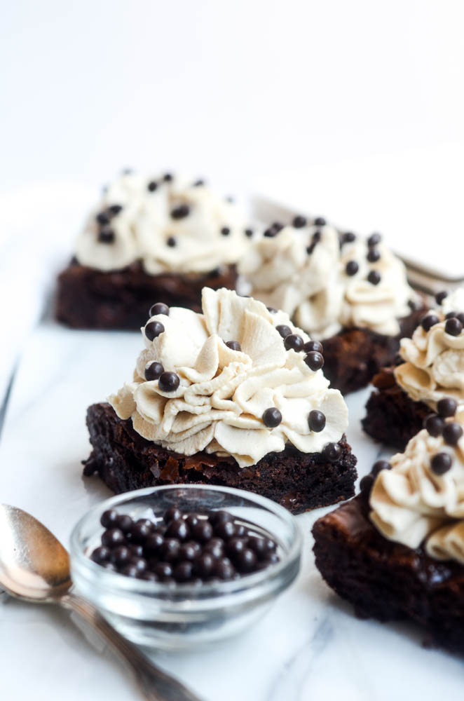 close up of one brownie with kahlua frosting and spoon and bowl of chocolate nibs