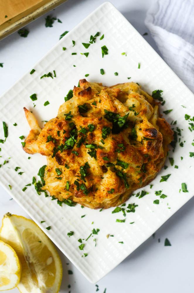 up close flat lay of crab cake on white  square plate with two lemon wedges next to plate