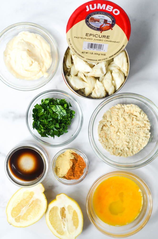 aerial shot of lots of bowls with ingredients: can of crab meat, mayonnaise, parsley, saltine crumbs, egg, old bay, dry mustard, worchestire, and lemon. 