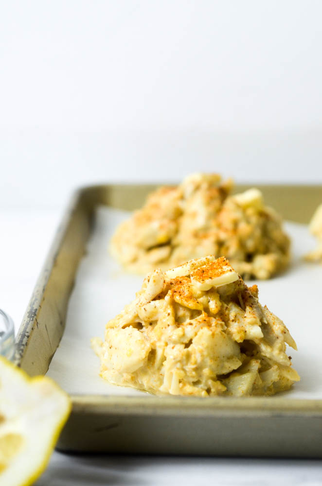 side shot of crab cake with pad of butter and old bay on top before going in the oven