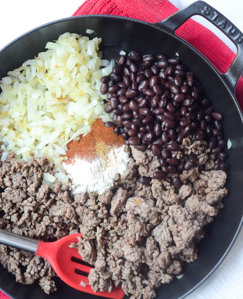 flatlay of skillet with ground beef, onions, black beans, and taco seasoning. 