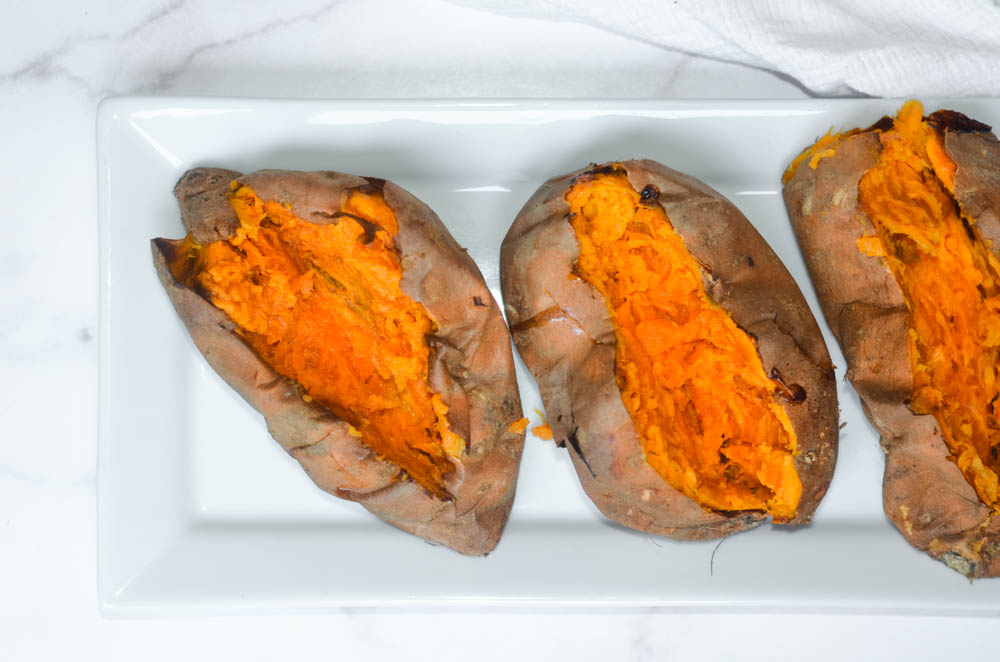 aerial photo of 3 baked sweet potatoes opened up on white tray