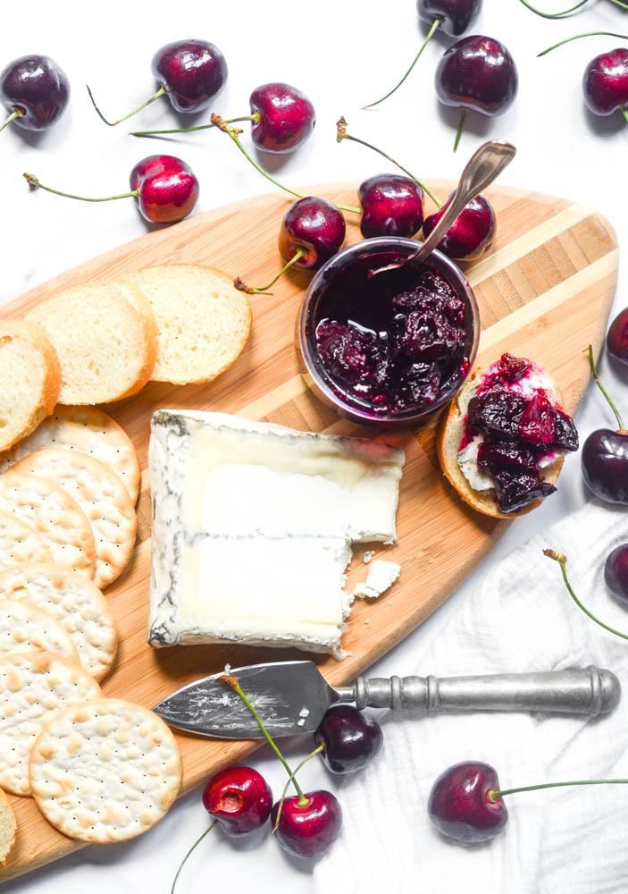 aerial view of wooden cutting board with cheese, crackers, bread, and cherry spread.