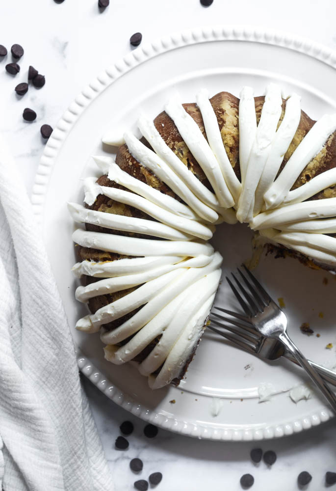 aerial shot of bundt cake on white platter after it's frosted with a few pieces missing