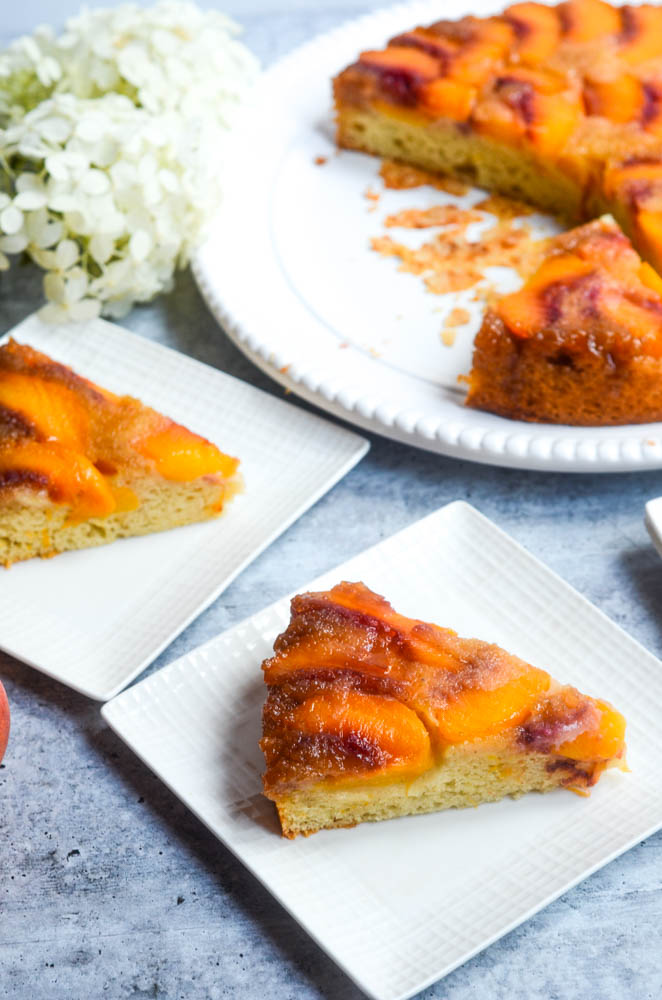 slice of peach cake on white plate with cake in background