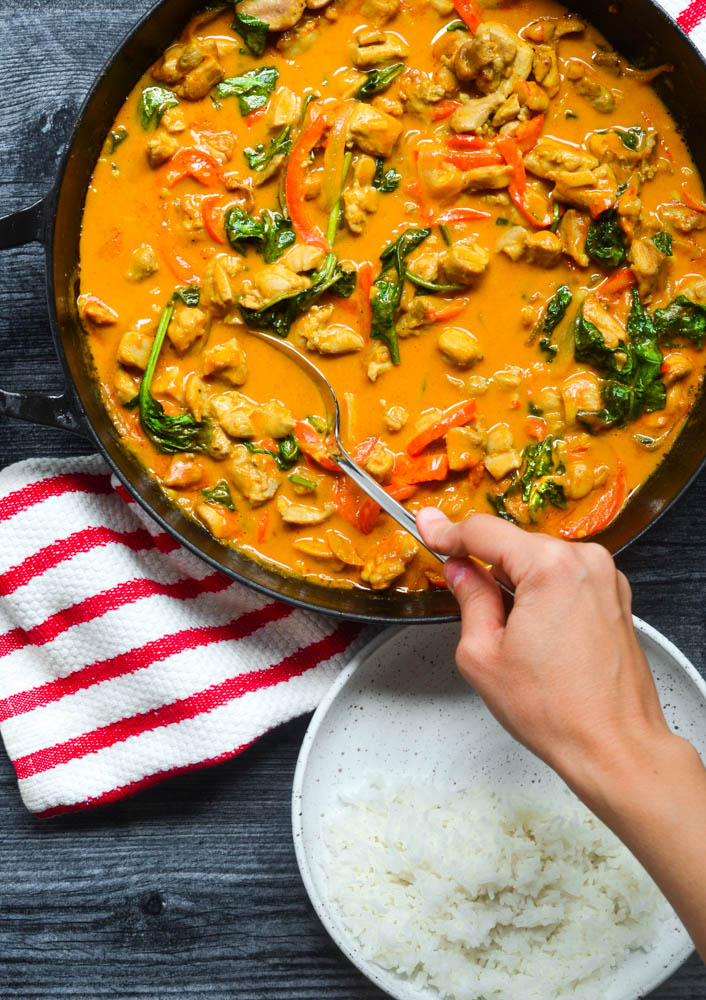 aerial picture of hand scooping up curry with a spoon ready to place on white plate with rice.