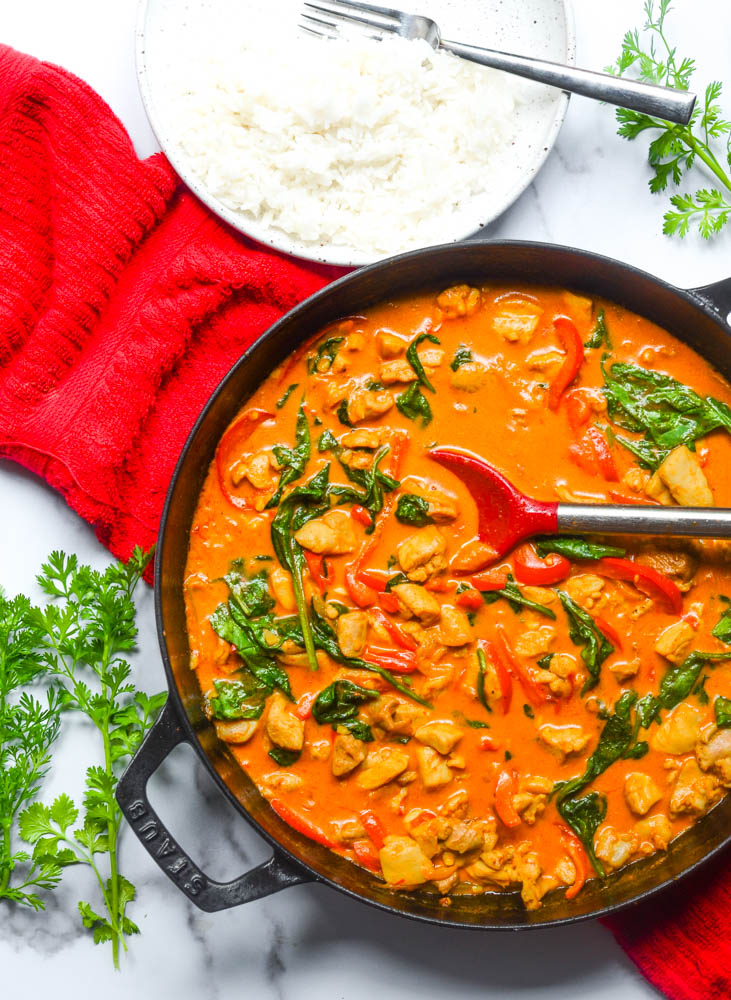 aerial shot of coconut curry chicken in black cast iron skillet with red dish towel draped under and cilantro next to pan