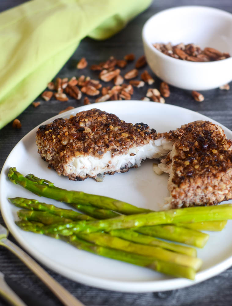 side view of fish encrusted with pecans on white plate with asparagus 