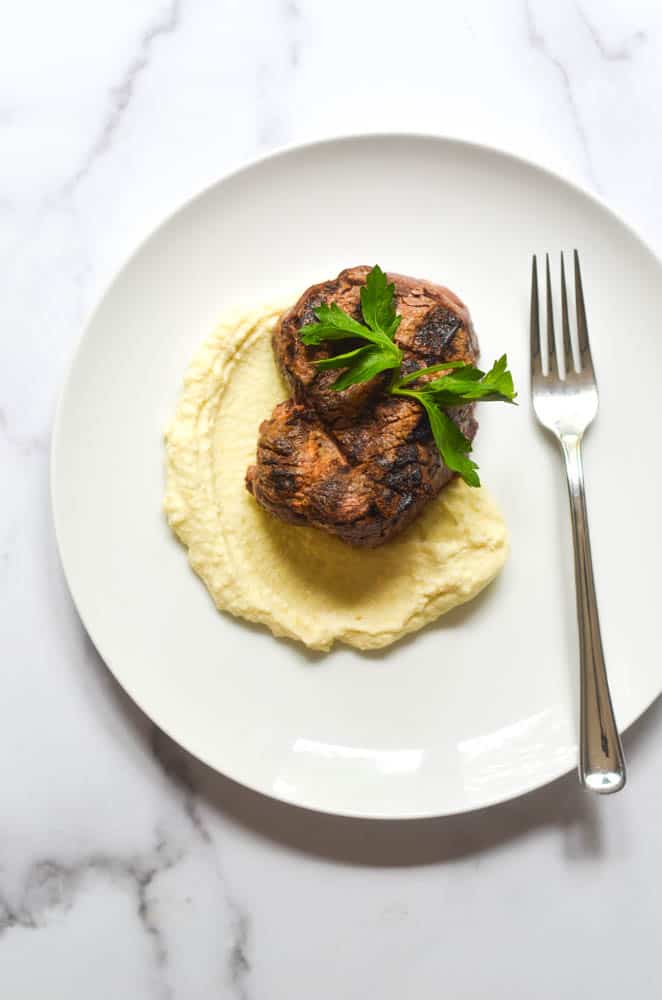 flatlay picture of fillet on bed of mashed potatoes all on white plate and white marble background