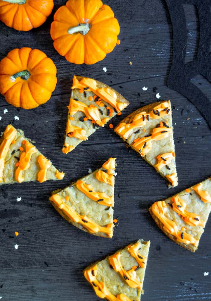 slices of cookie cake on black backdrop with sprinkles and three pumpkins scattered.