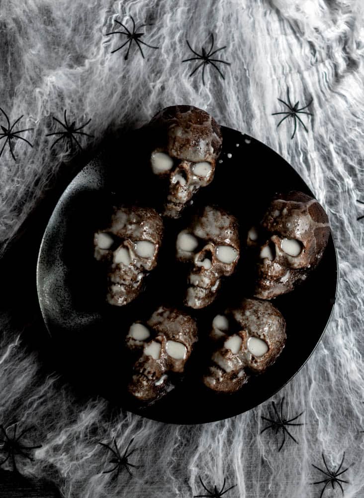 aerial photo of 6 skull chocolate cakes on black plate on top of spider web. 