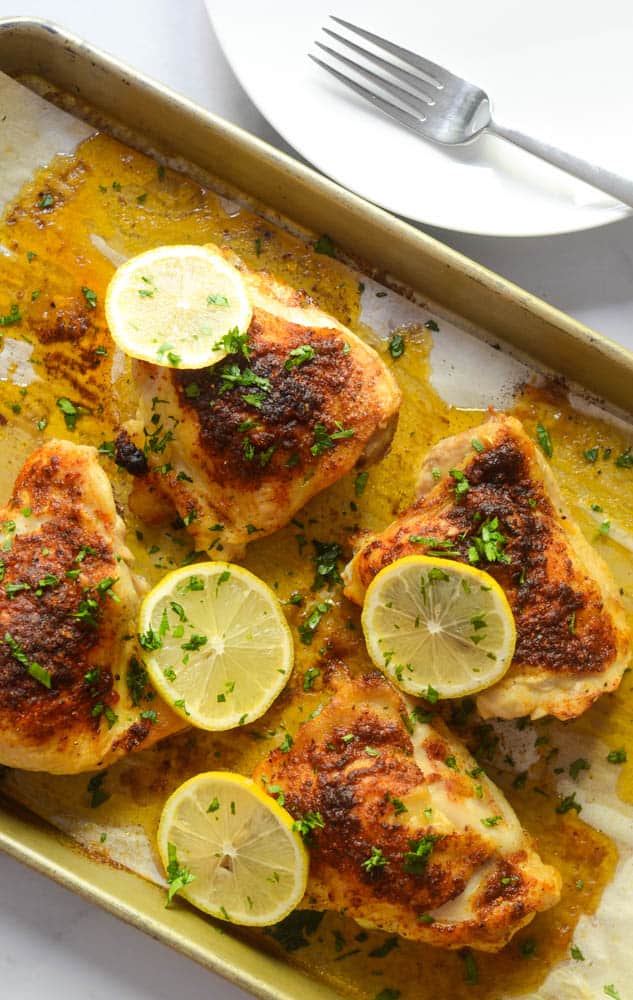 overhead picture of sheet pan with roasted chicken thighs garnished with parsley and lemon slices.