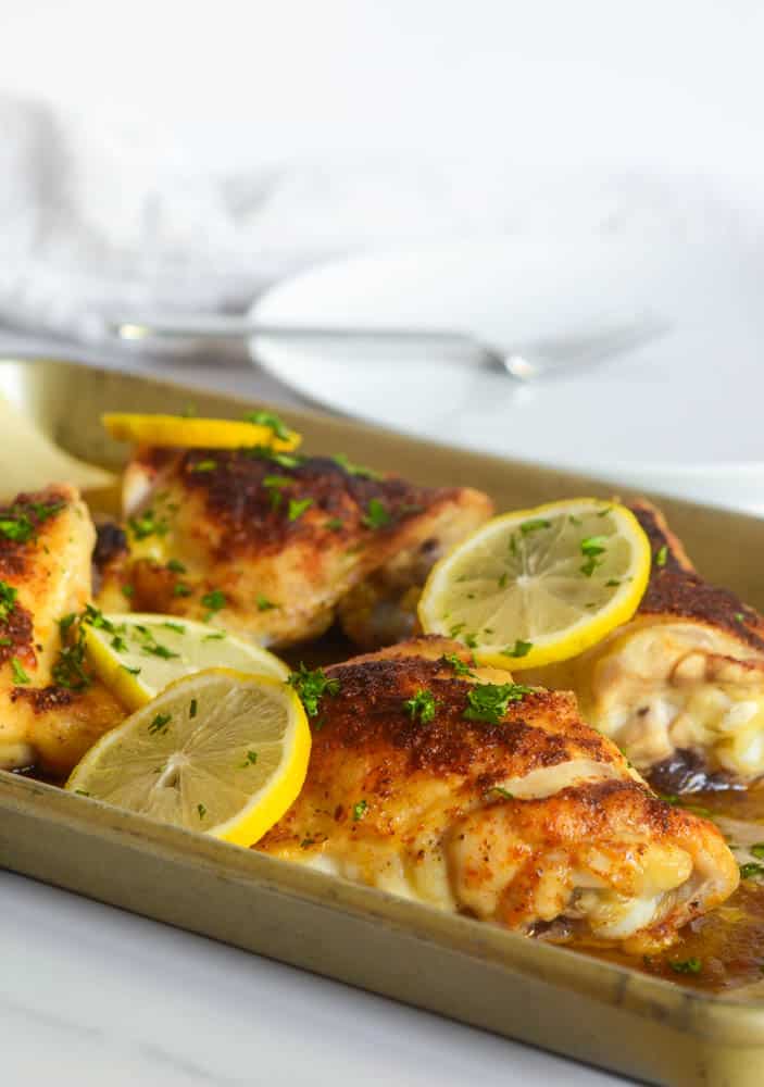 up close picture of roasted chicken thigh garnished with parsley and lemon slices. 