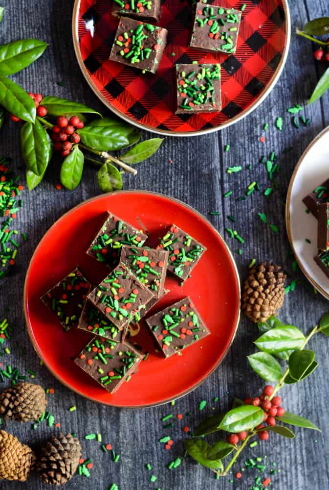 aerial photo of 2 plates with small squares of chocolate fudge stacked on them with holly and pine cones strewn about. 