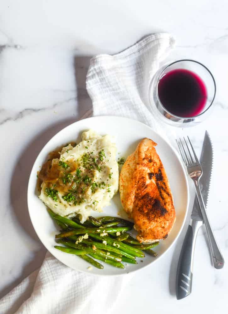 aerial view of whit eplate with green beans, mashed potatoes and gravy, and chicken breast with a glass of red wine. 