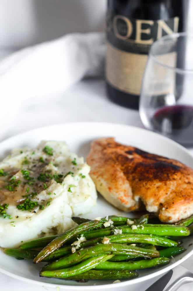 close up picture of white plate with green beans and garlic on top. Mashed potatoes and chicken are in the background. 