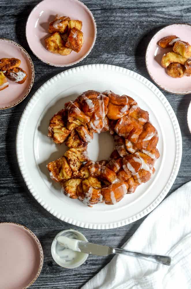 flat lay of white platter holding monkey bread on black background surrounded by light pink plates with pieces of bread on them. 