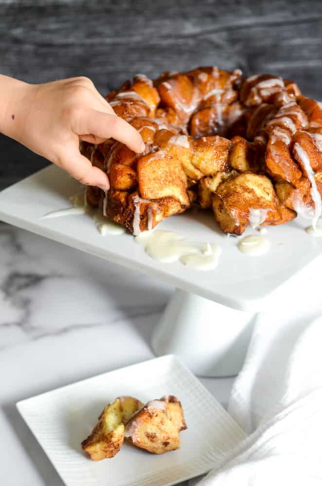 small child's hand pulling a piece of the cinnamon roll off the monkey bread. 