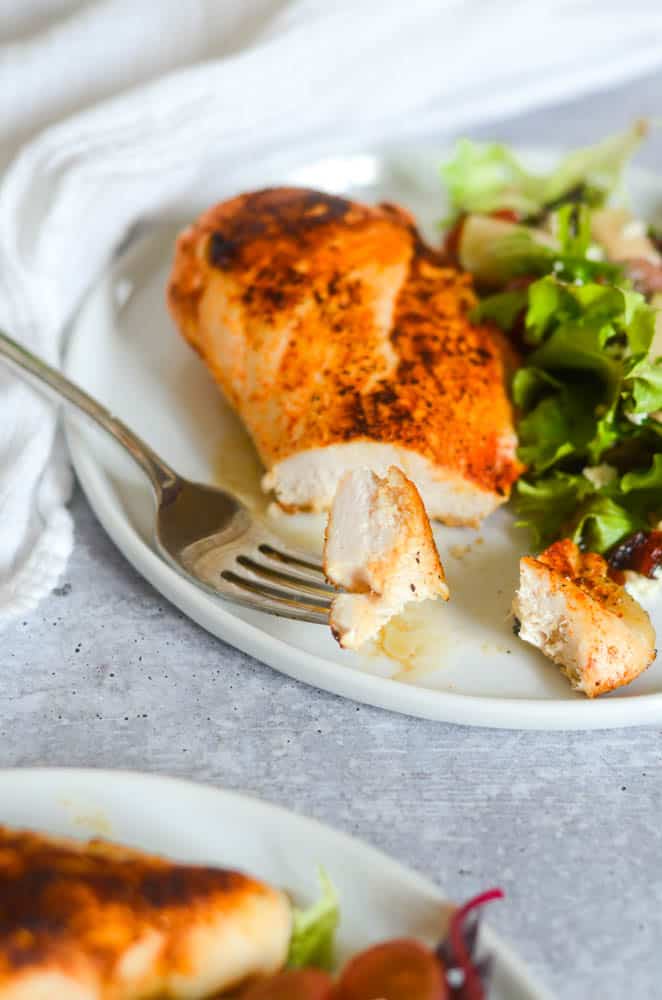 close up of fork with bite of cut chicken with rest of plate in the background.