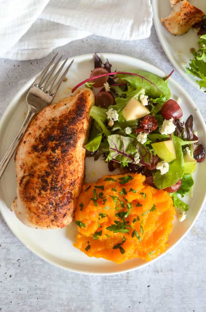 aerial picture of chicken breast, side salad, and butternut squash mash on white plate.