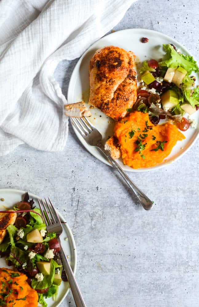 two white plates with chicken breast, butternut squash mash, and salad against concrete background. 