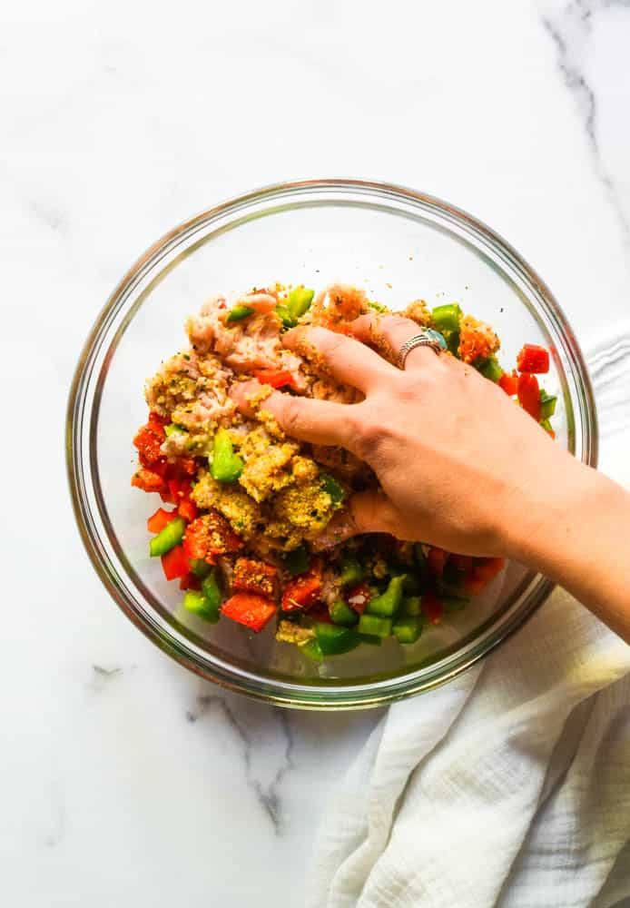 hand mixing the chicken burger ingredients in a glass bowl. 