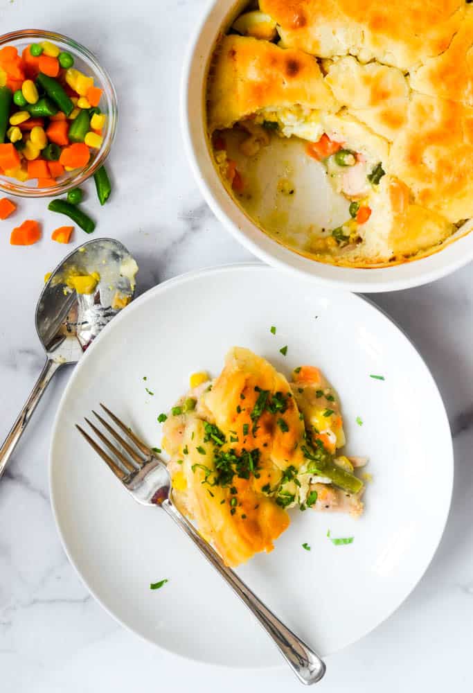 overhead picture of scoop of chicken pot pie on white plate next to casserole dish of chicken pot pie. 