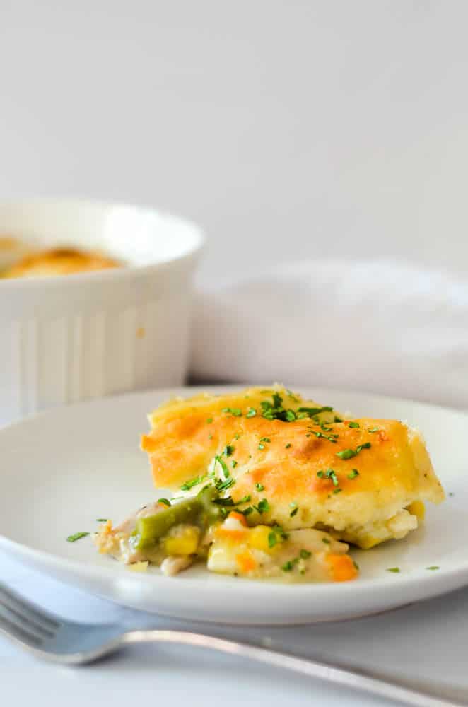 close up picture of scoop of chicken pot pie on white plate with fork in front of plate. 