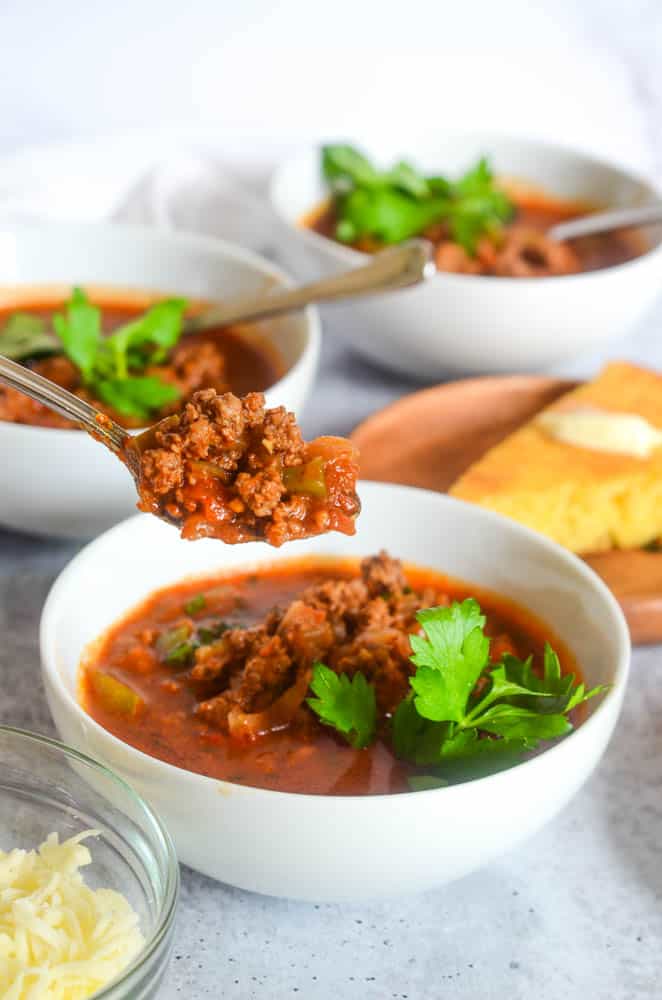 spoonful of chili on a spoon with 3 bowls of chili and a cornbread visible in the background. 