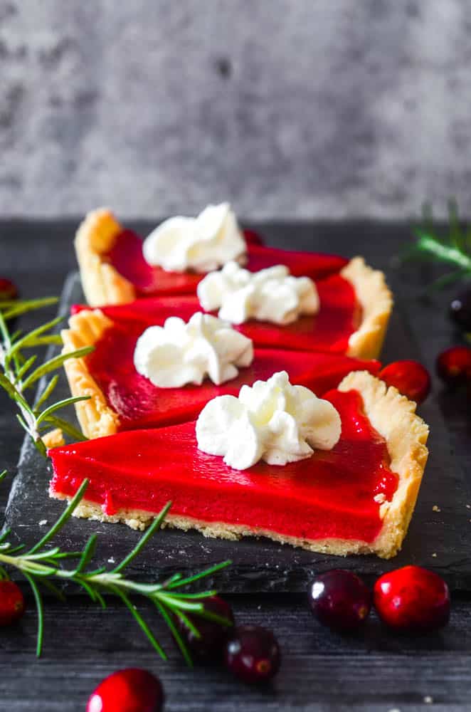 side view of cranberry curd tart slices around rosemary sprigs and loose cranberries.