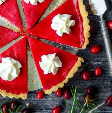 cranberry curd tart slices with dollop of whipped cream and cranberries scattered along black background with cranberries loose.