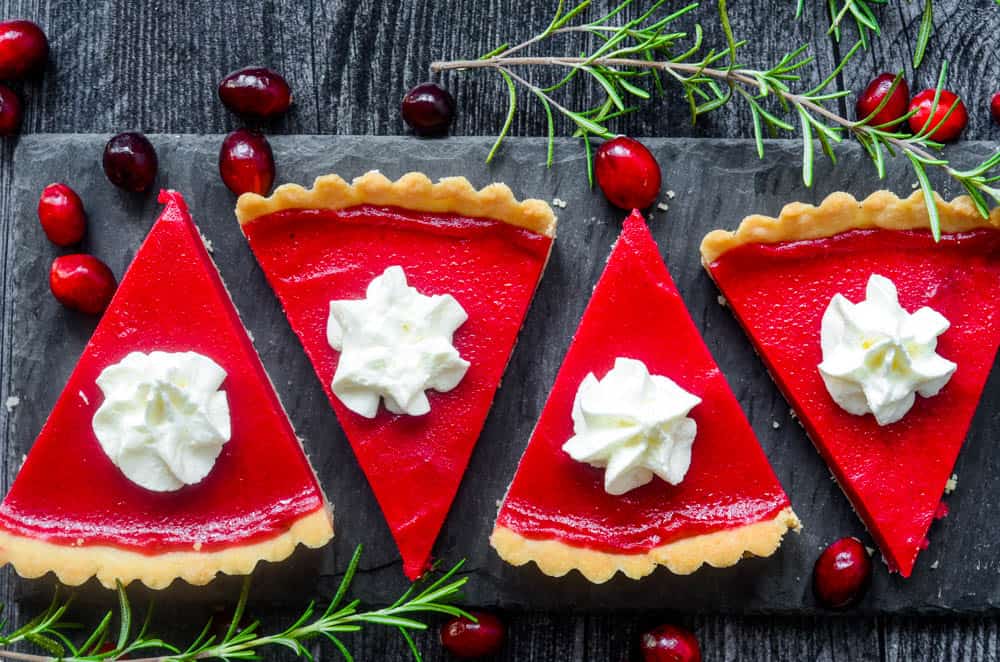 horizontal picture of slices of cranberry curd tart cut on black slate plate with rosemary and cranberries. 