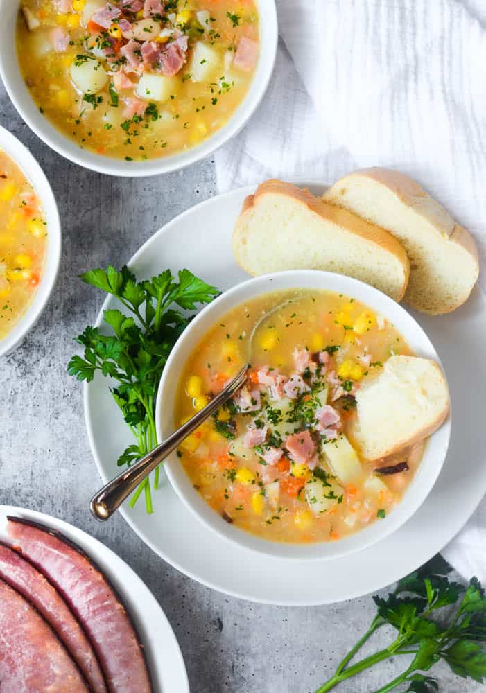 aerial picture of bowl of ham soup with plate of ham in the corner and two other bowls in the upper corner. 