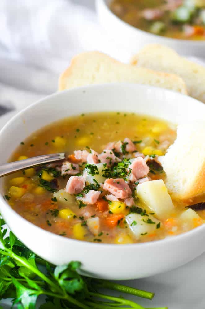 side angle of a bowl of ham soup with ham, corn, potatoes visible and garnished with parsley. 